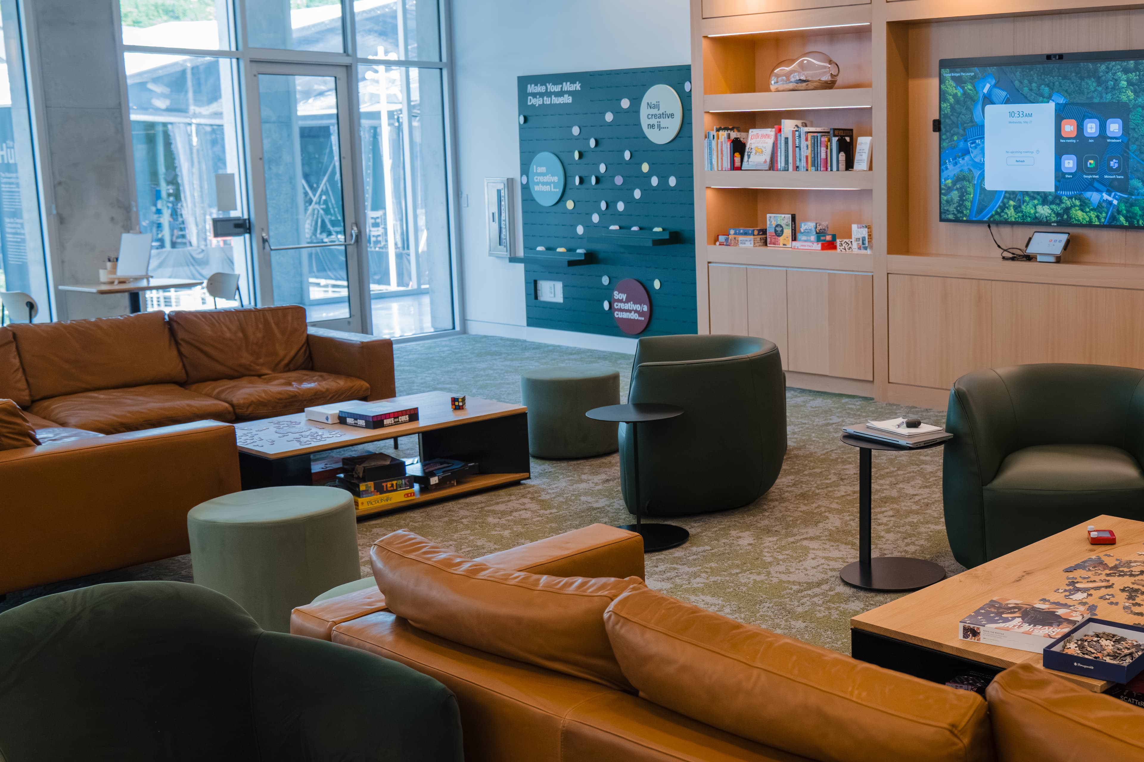 A lounge with bookshelves, digital screen, and seating around tables topped with puzzles and games.