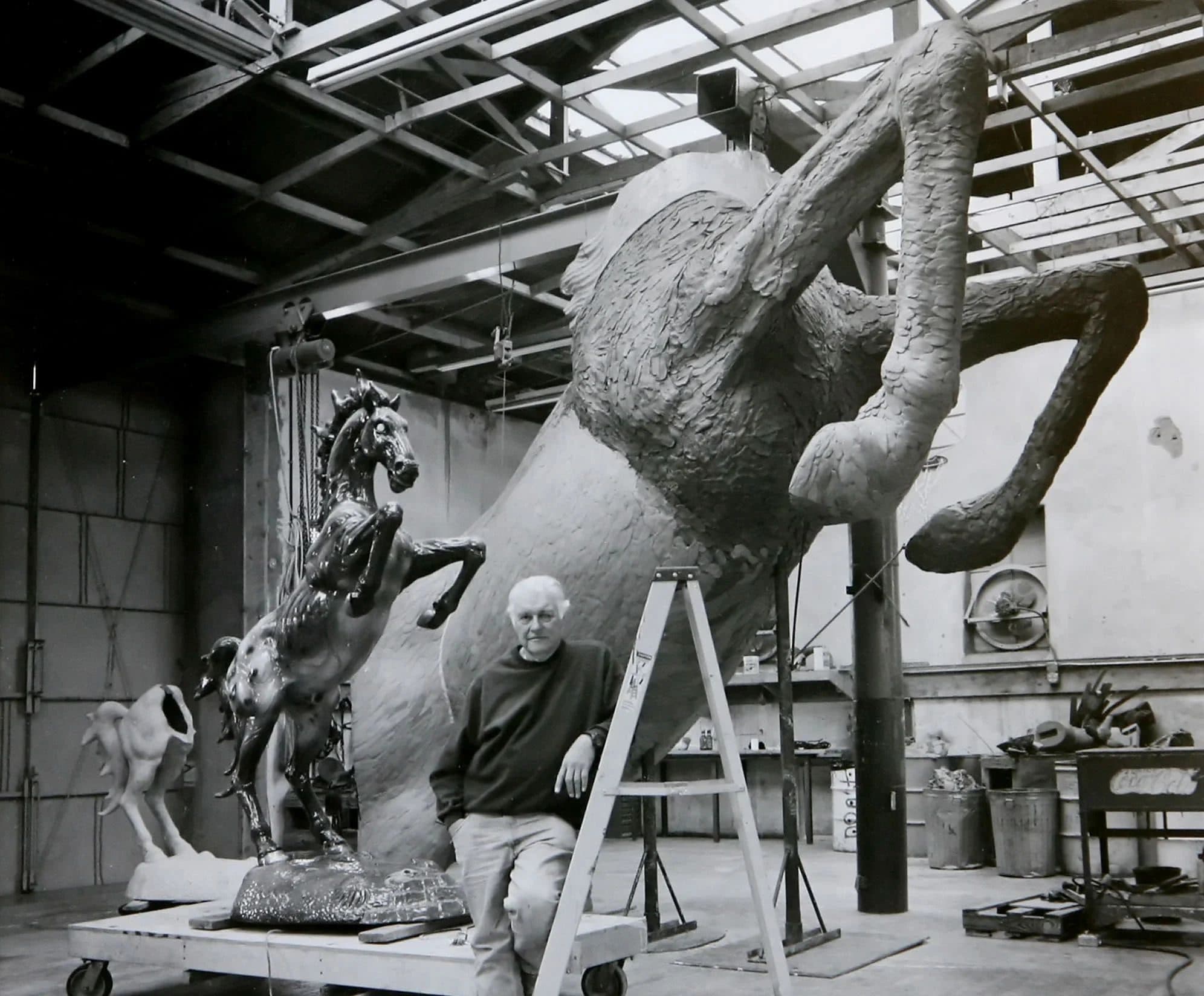 Man beside large horse sculptures in industrial workshop